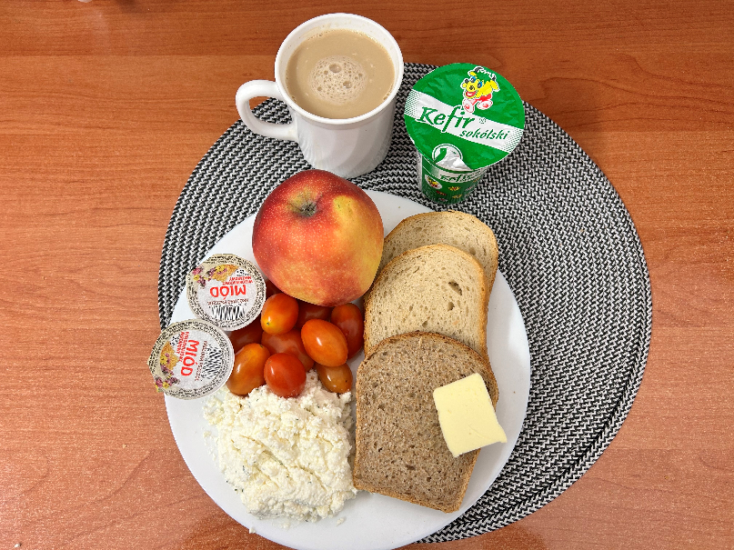 Na zdjęciu znajduje się: Kefir 2%, Kawa zbożowa z mlekiem, Chleb mieszany pszenno-żytni, Chleb Graham, Masło extra 82%, Miód, Twarożek, Jabłko, Pomidorki koktajlowe